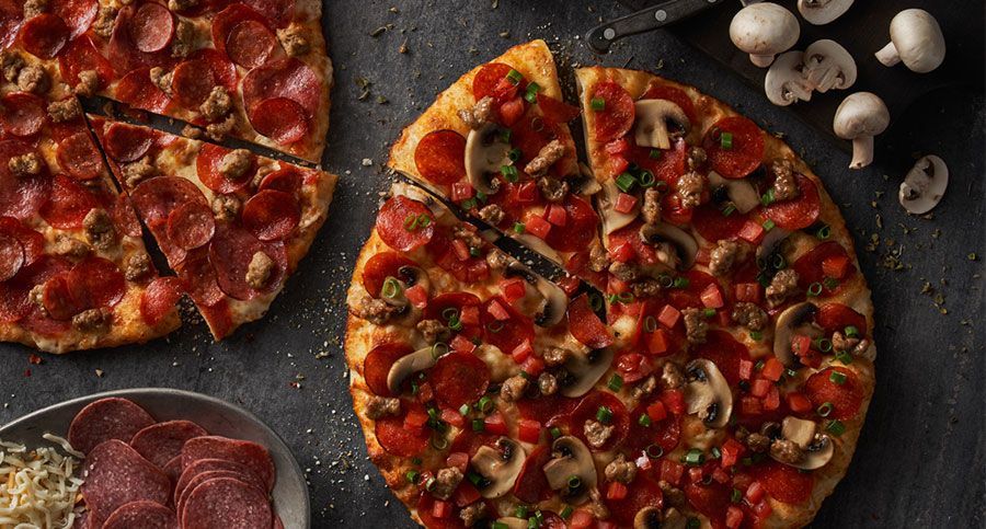 A pizza with pepperoni , mushrooms , and cheese is sitting on a table.