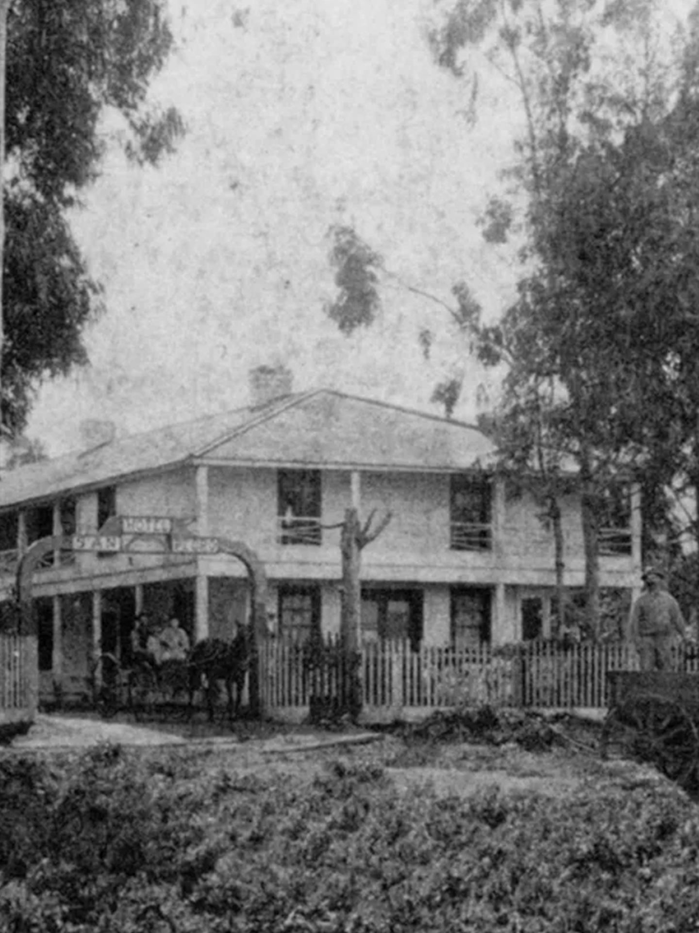 A black and white photo of a house with a horse drawn carriage in front of it.