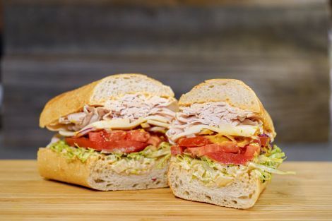 A sandwich is cut in half on a wooden cutting board.