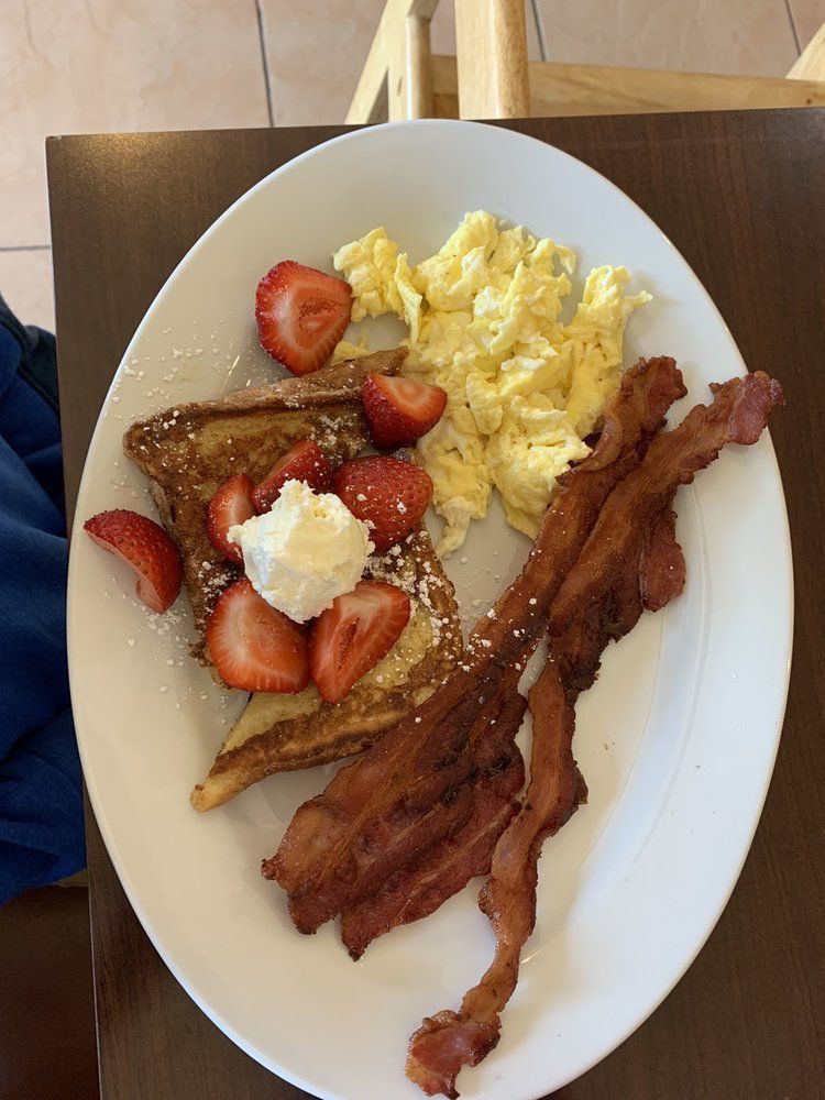 A white plate topped with french toast eggs bacon and strawberries