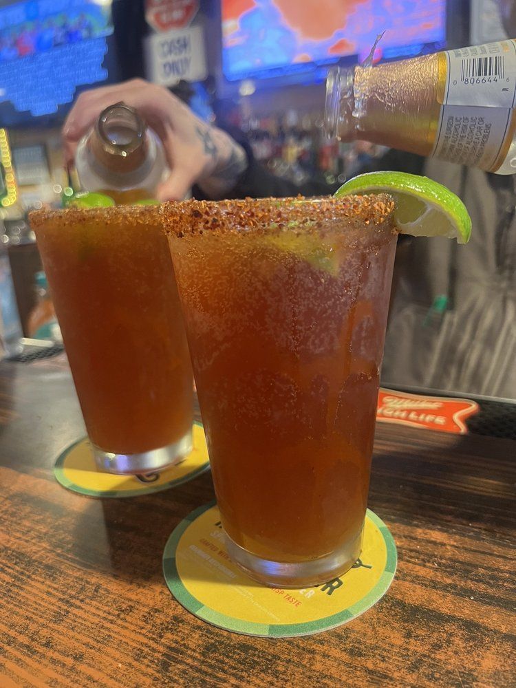 A person is pouring a drink into two glasses on a bar.