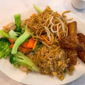 A white plate topped with noodles , rice , broccoli , carrots and chicken wings.