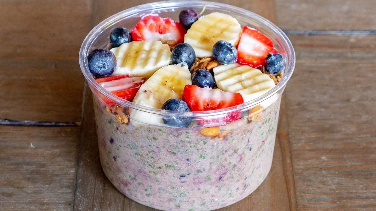 A bowl of oatmeal with bananas , strawberries , blueberries and granola on a wooden table.