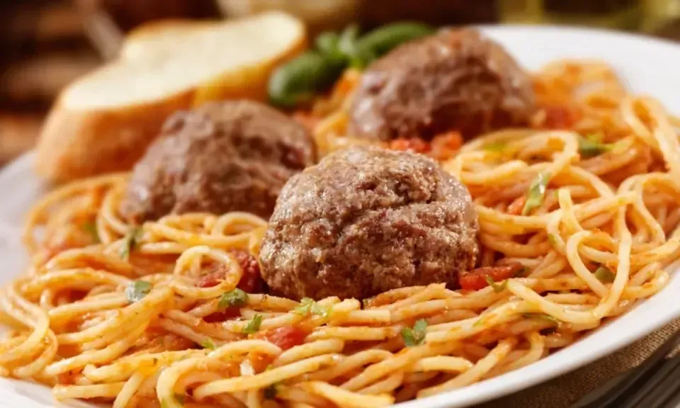 A plate of spaghetti and meatballs with a piece of bread on the side.