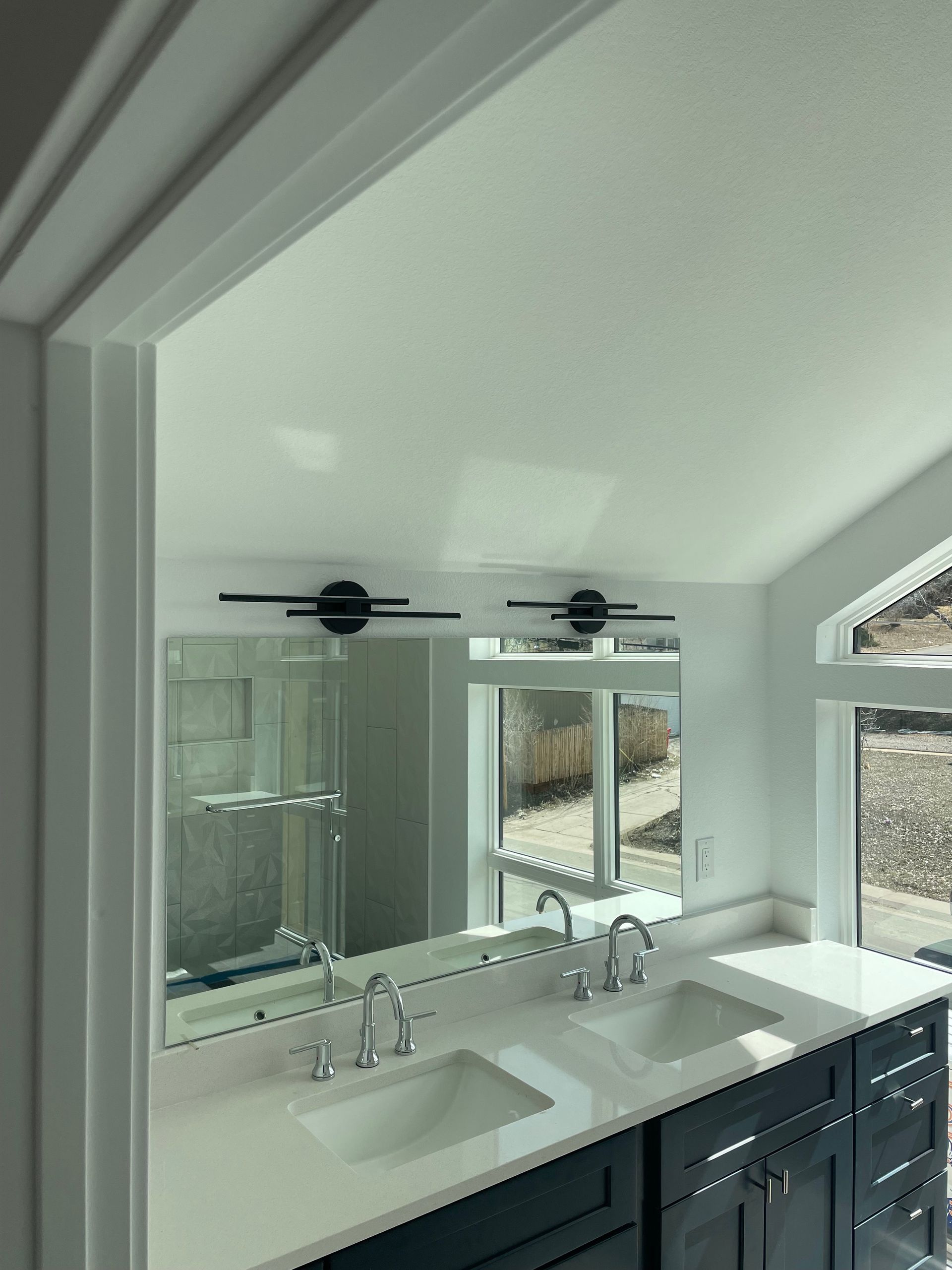 Modern bathroom with a large mirror over a double vanity, window to the right.