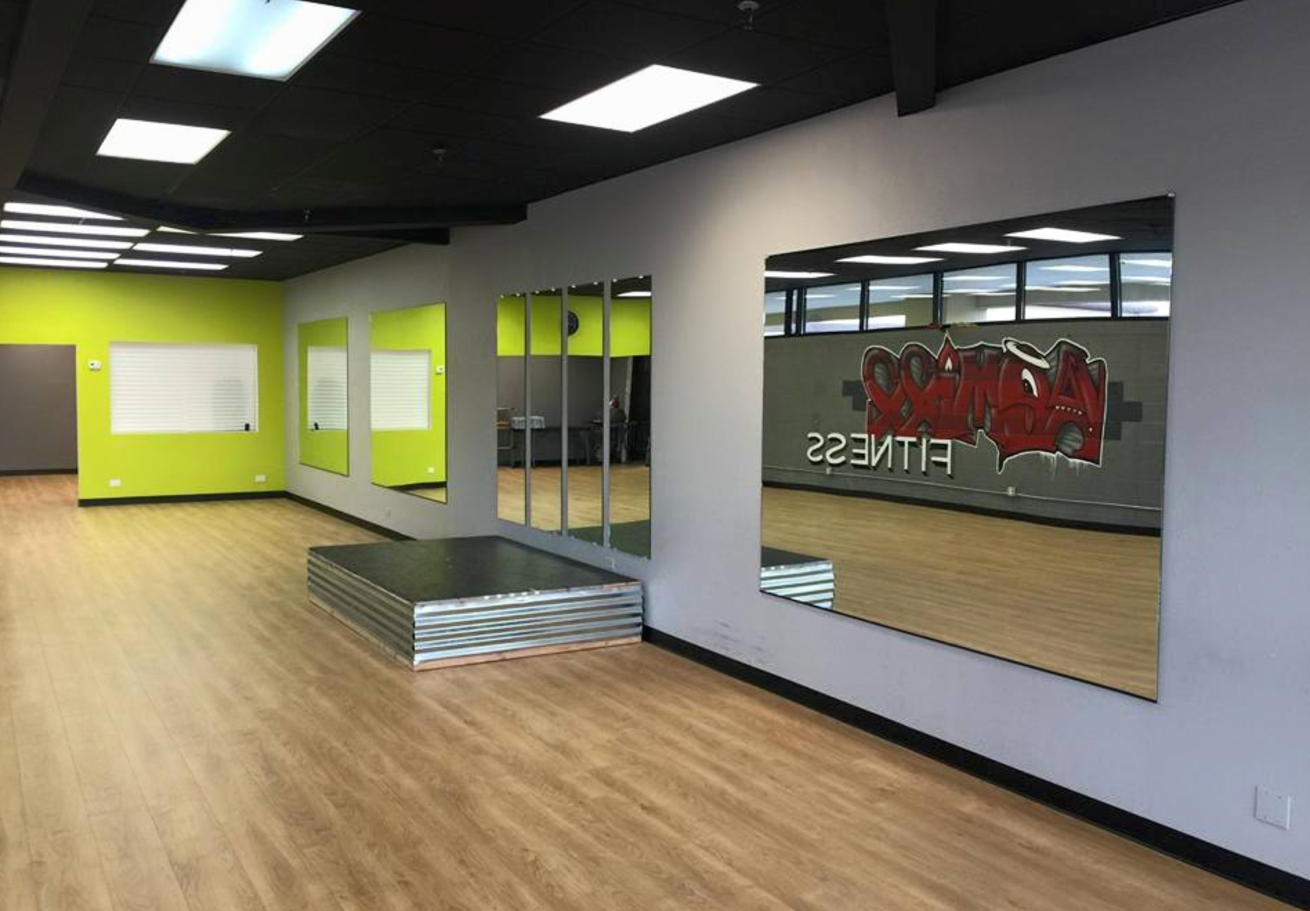 Empty fitness studio with mirrors, wooden floor, and green and gray walls.