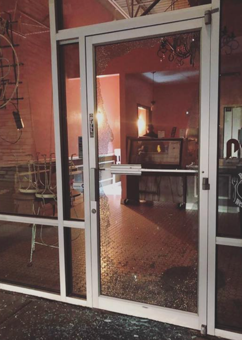 Shattered glass door of a building. Interior shows a room with pink walls and a desk.