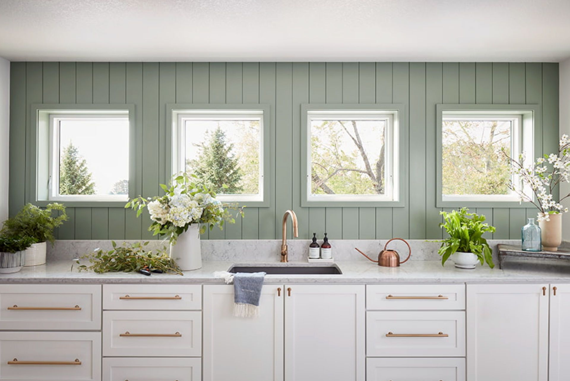 White kitchen with sage green wall paneling, white cabinets, and four windows.