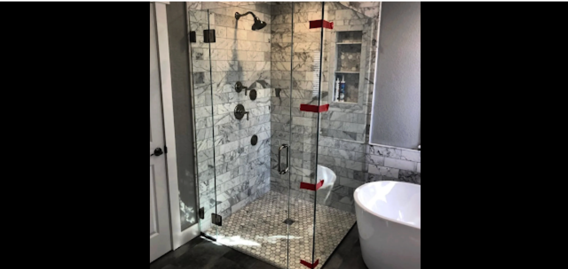 Bathroom with a glass shower enclosure with red hinges, marble tile, and a standalone tub.