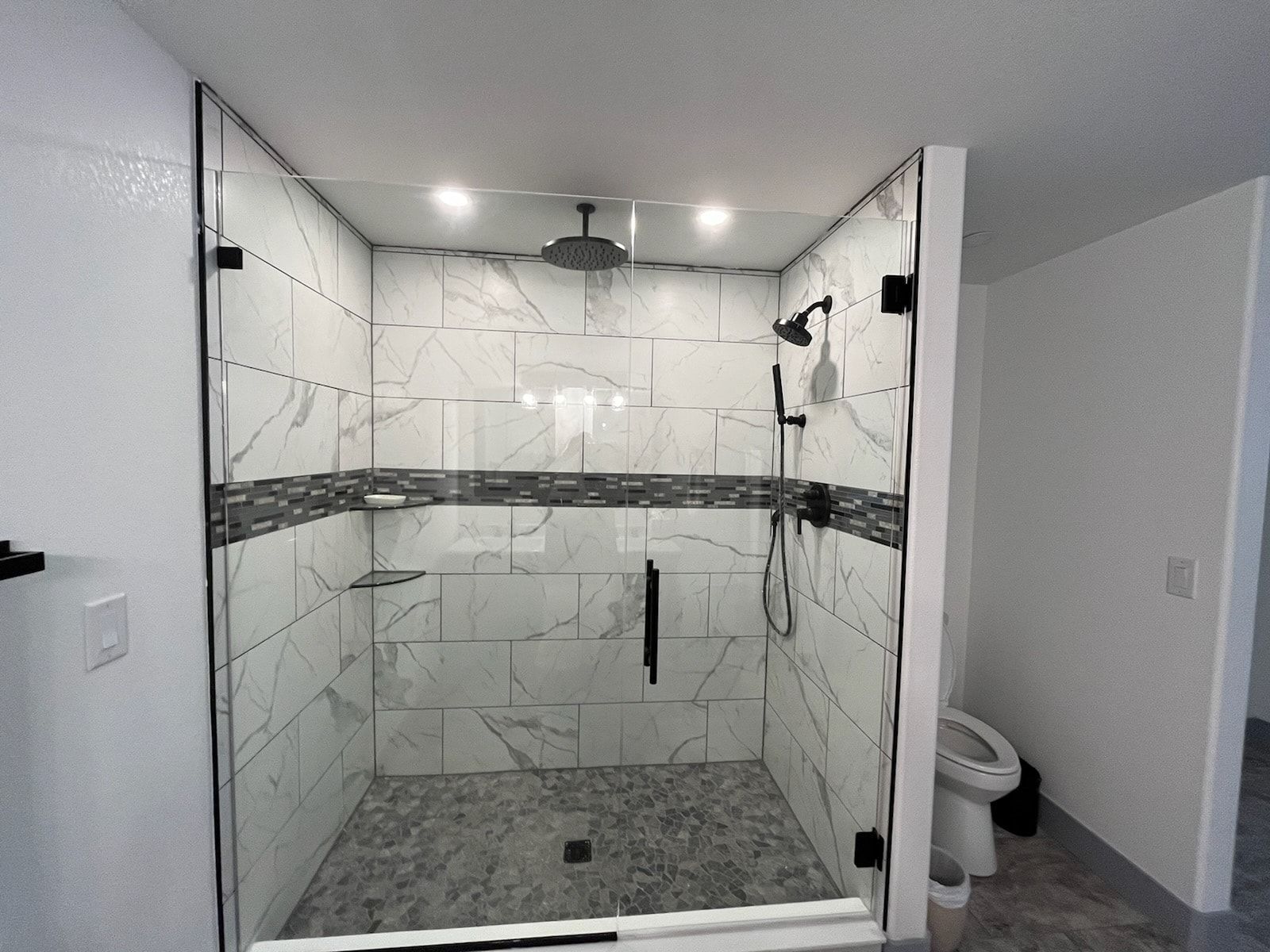 Modern tiled walk-in shower with glass doors and rainfall showerhead in a bright bathroom