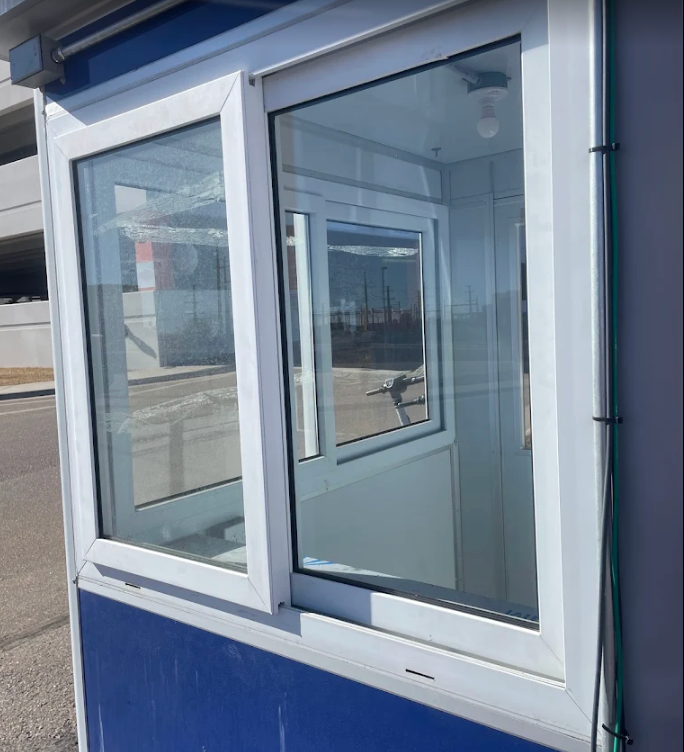 Blue and white security booth with glass windows and a smaller window for transactions.