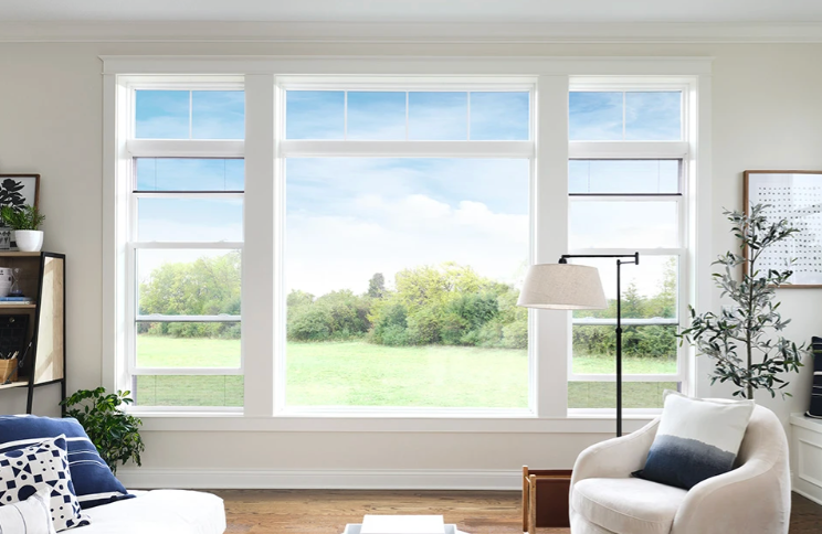 Bright, airy living room with large white-framed windows overlooking a green field and blue sky.