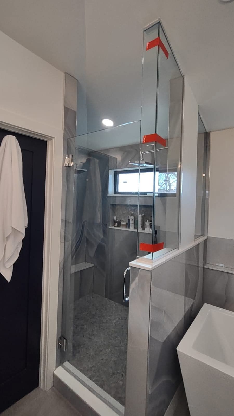 Modern bathroom with glass shower, gray tiles, white sink, and red accents.