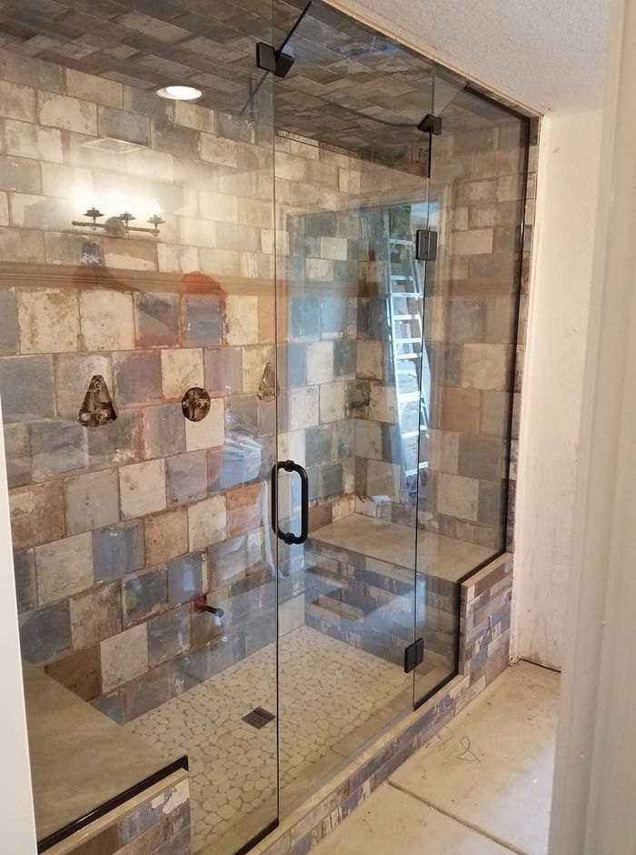 Glass shower enclosure with stone tile walls and a black handle.