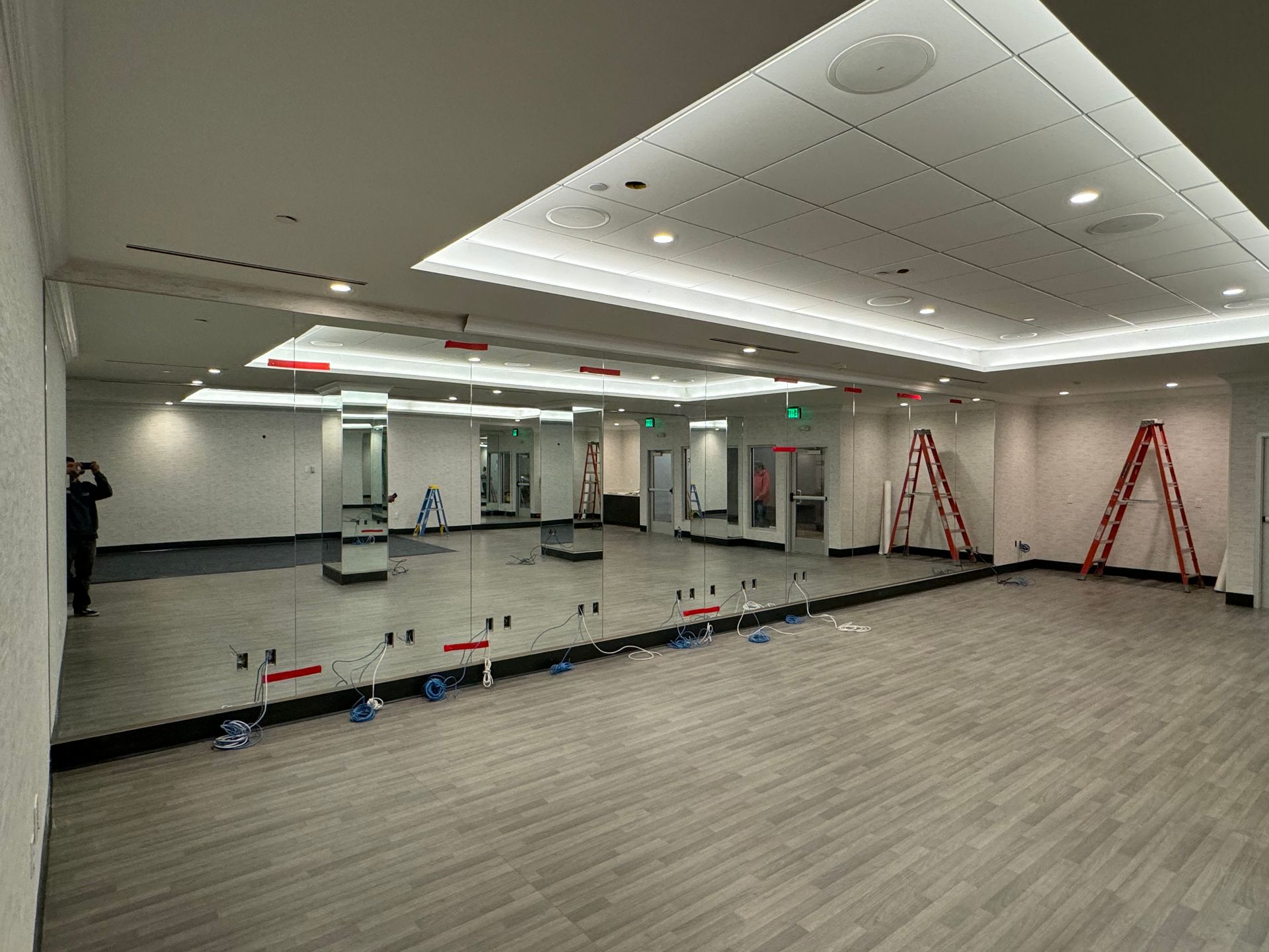 Large room with floor-to-ceiling mirrors, grey flooring, and red ladders against the wall.