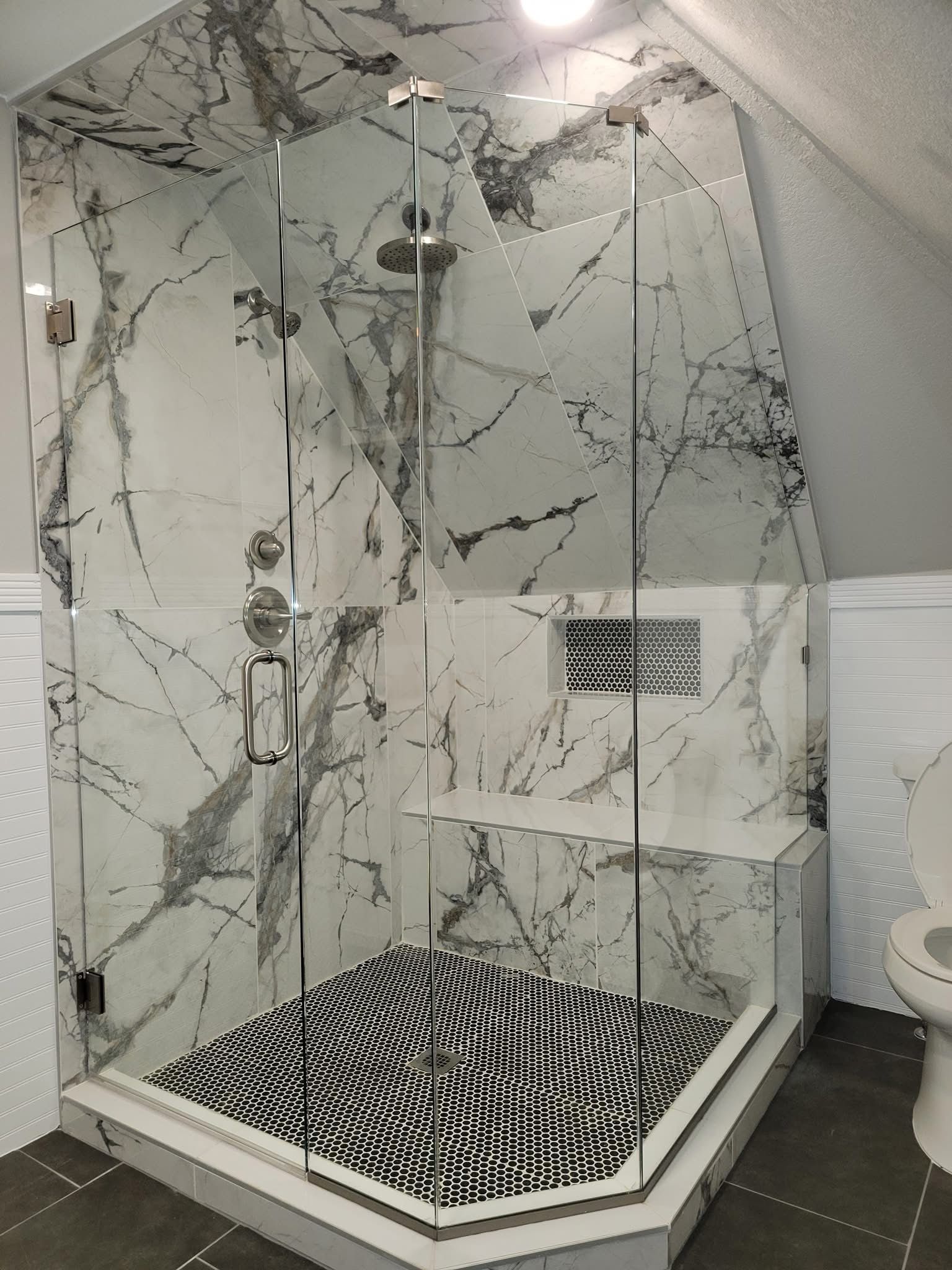 Glass shower with marble-patterned walls, a black and white patterned floor, and chrome fixtures.