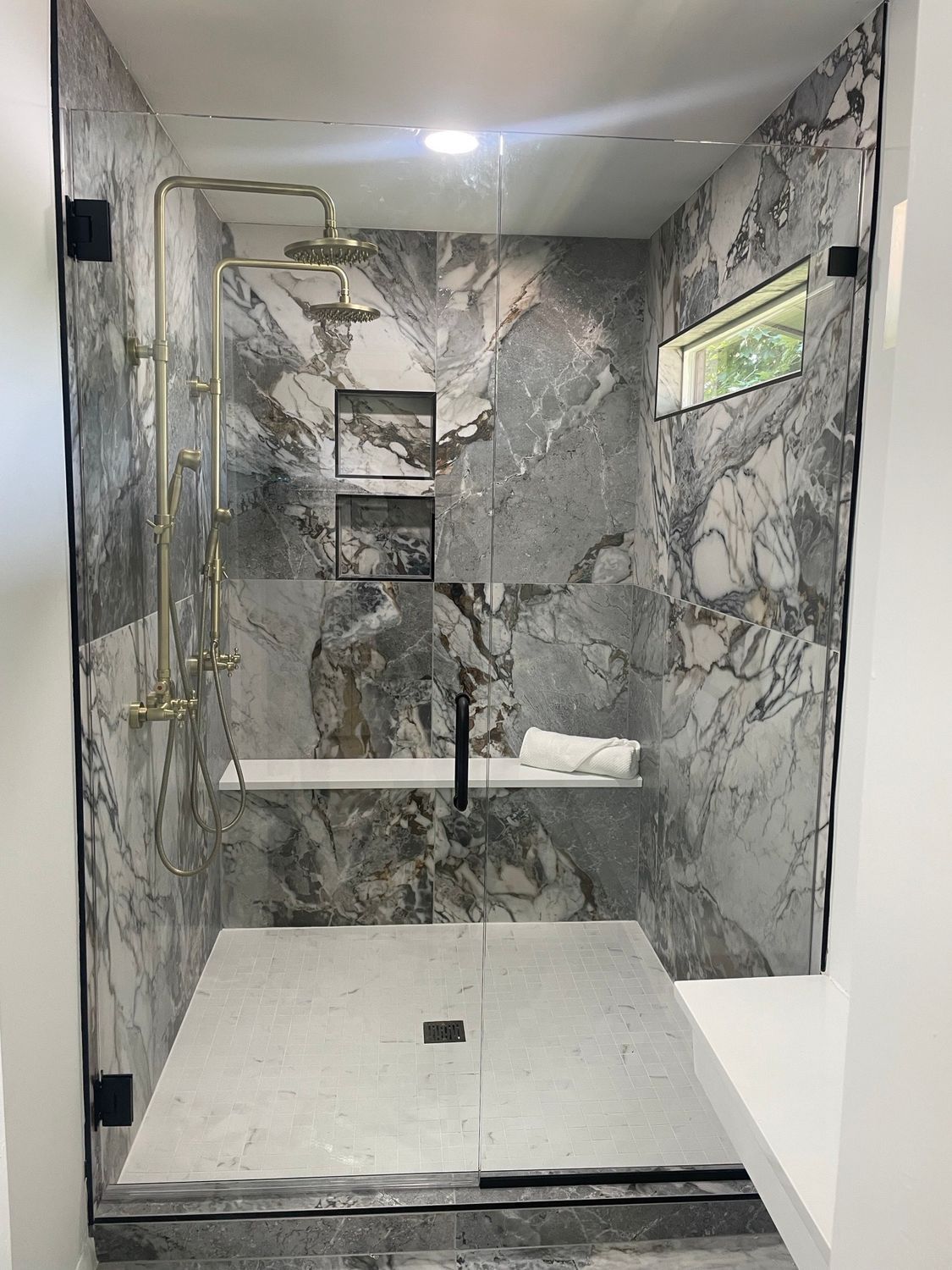 Luxurious marble shower with brass fixtures, a built-in bench, and glass doors.
