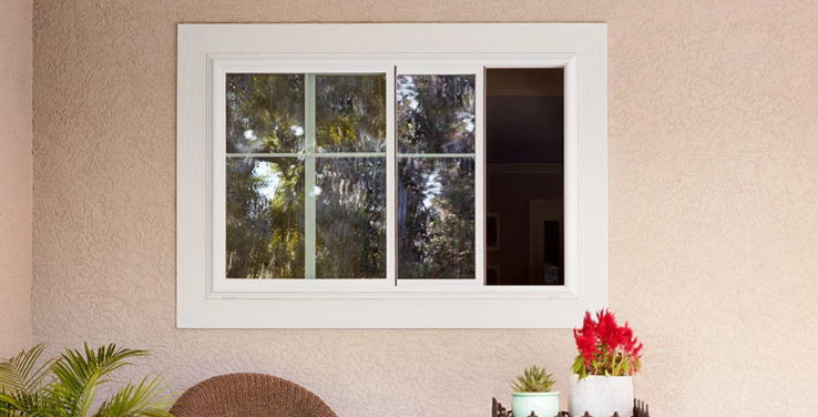 White-framed sliding window with trees reflected in it. A dark, closed panel is on the right. Red flowers on a table.