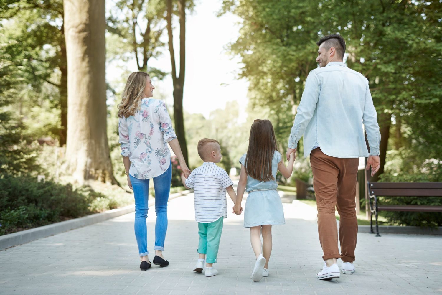 A family of four walks down a path in a park, holding hands.