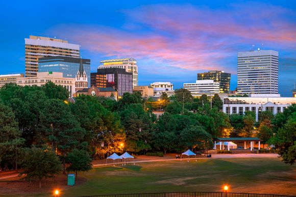 Skyline of Columbia, SC, at dusk, with buildings of varying heights and green park in foreground.
