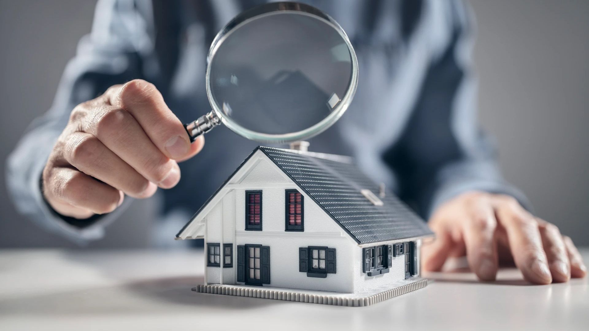 A person is looking at a model house with a magnifying glass.