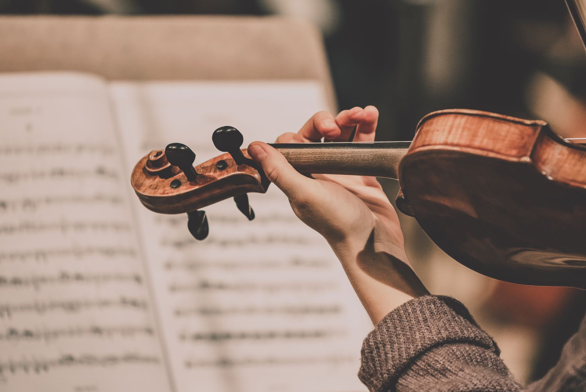 Hand playing a violin in front of sheet music on a stand