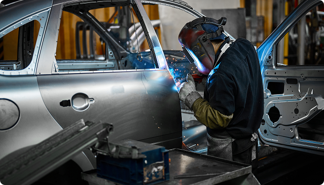 A man is welding a car door in a factory. | Morrison Corp Mobile Body & Paint