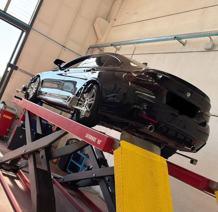 Auto sportiva nera su un sollevatore idraulico rosso all'interno di un'officina.