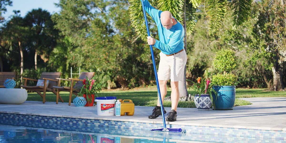 A man is cleaning a swimming pool with a mop.