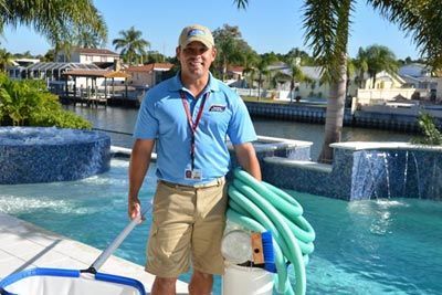 A man is standing next to a pool holding a hose and a bucket.