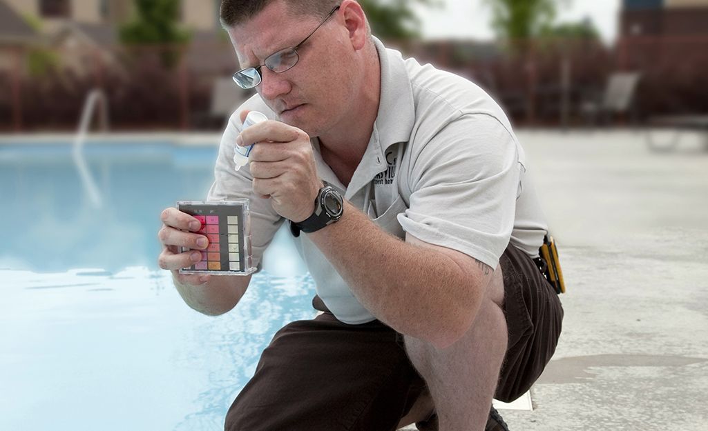 A man is kneeling down next to a swimming pool looking at the water.