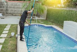 A man is cleaning a swimming pool with a broom.