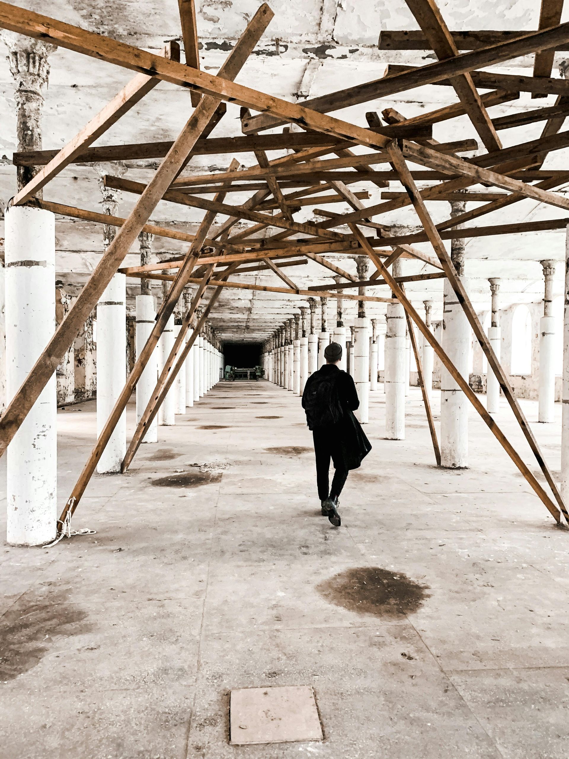 A man is walking through a long hallway with wooden beams.
