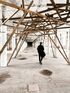 A man is walking through a long hallway with wooden beams.