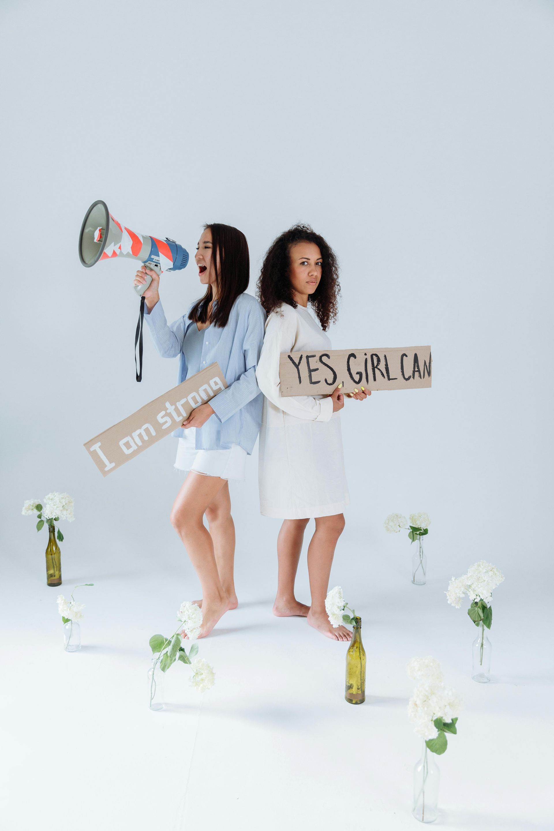 Two women are standing back to back holding signs and a megaphone.