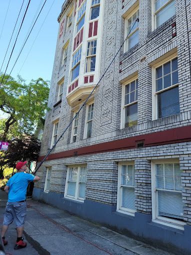 A man is cleaning the windows of a large brick building.