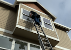 A man is standing on a ladder on the side of a house.