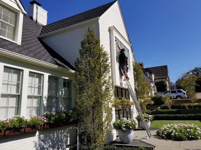 Expert window cleaner on a ladder providing residential window cleaning services for a Portland home.