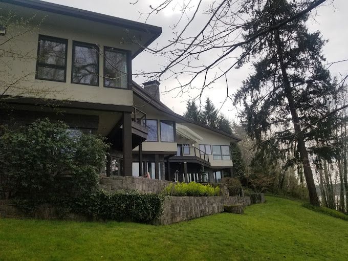 A large house is sitting on top of a lush green hillside surrounded by trees.