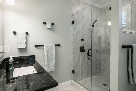A modern bathroom with a black granite vanity, white sink, matte black hardware, and a marble-tiled glass shower.