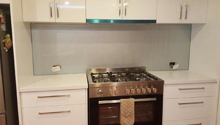A modern kitchen with a gas stove, white cabinets, and a gray glass splashback.