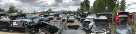 A wide panoramic view of a junkyard with numerous wrecked vehicles under a cloudy sky.