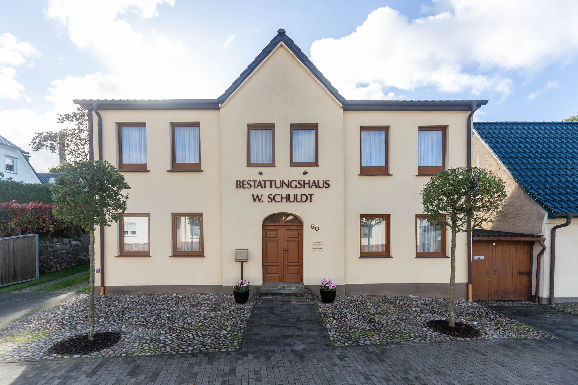 Zweistöckiges beiges Gebäude mit braunen Türen, Fenstern und der Aufschrift „BESTATTUNGSHAUS W. SCHULDT“.