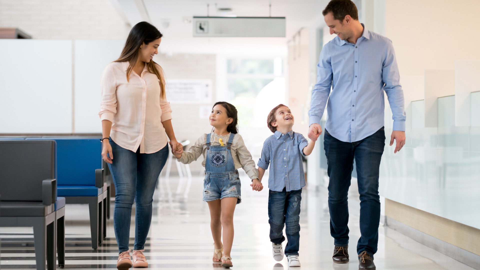 A family is walking down a hospital hallway holding hands.