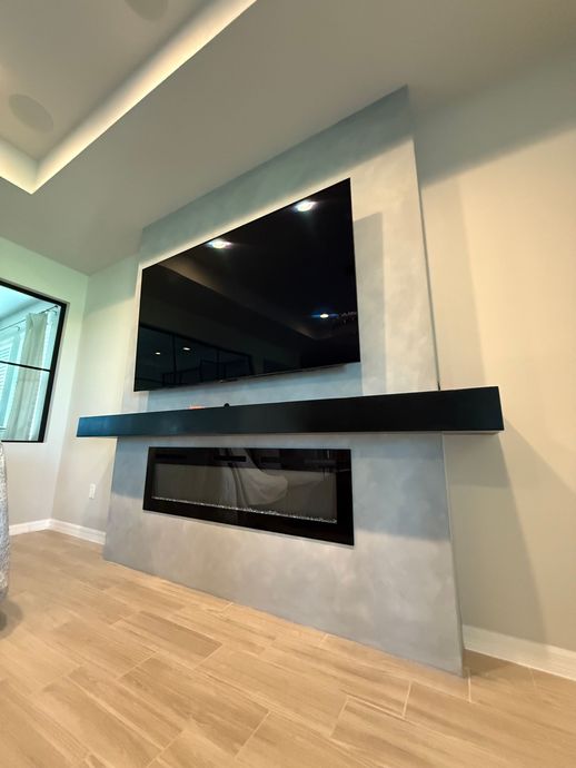 Modern fireplace with built-in TV and black mantel. Gray wall surround, beige flooring.