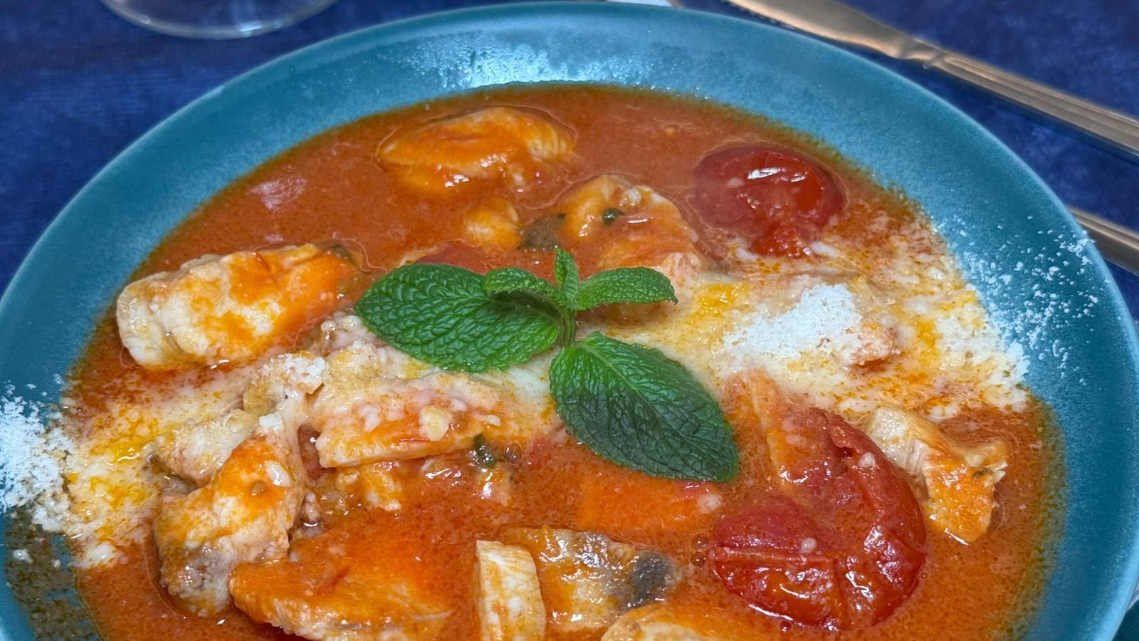 Ciotola di stufato di pesce con pomodori, formaggio e menta.
