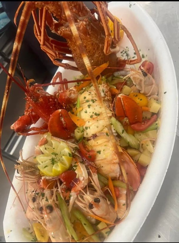 Piatto di frutti di mare: aragosta, gamberi e verdure in una ciotola bianca.