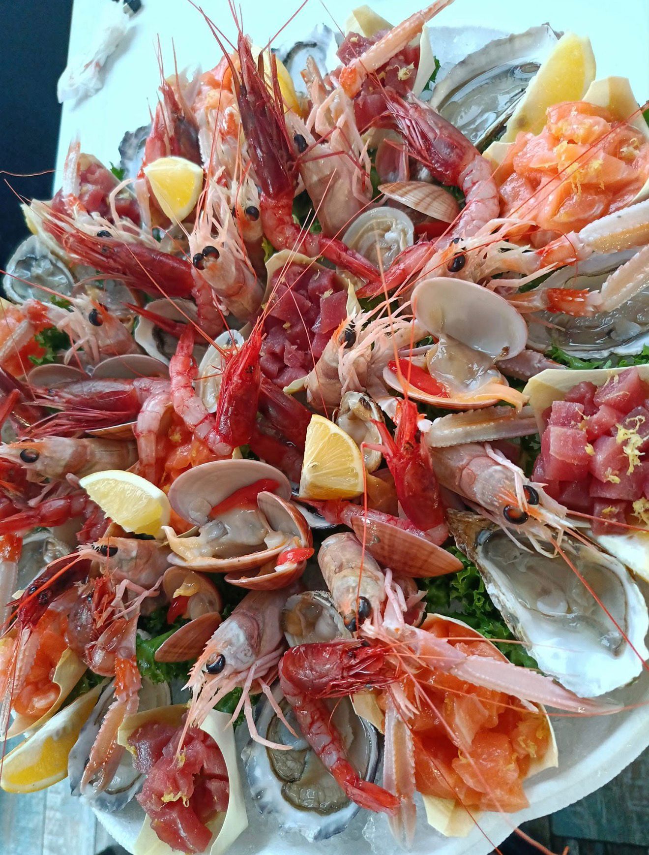 Piatto di frutti di mare con gamberi, ostriche, vongole e tonno, guarnito con fette di limone.