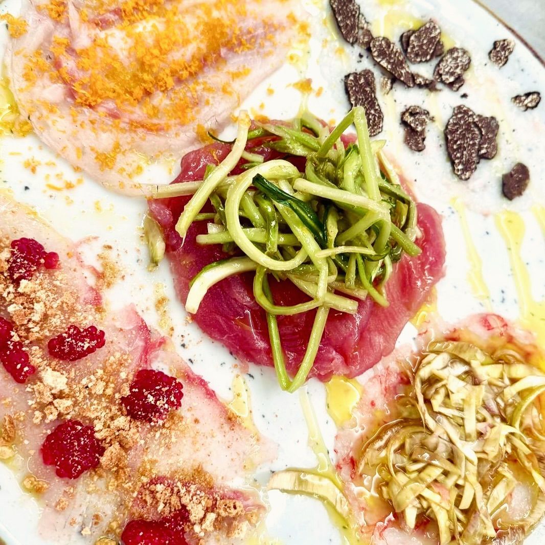 Carpaccio di frutti di mare misti: tonno crudo con zucchine e altri pesci con guarnizioni su un piatto bianco.