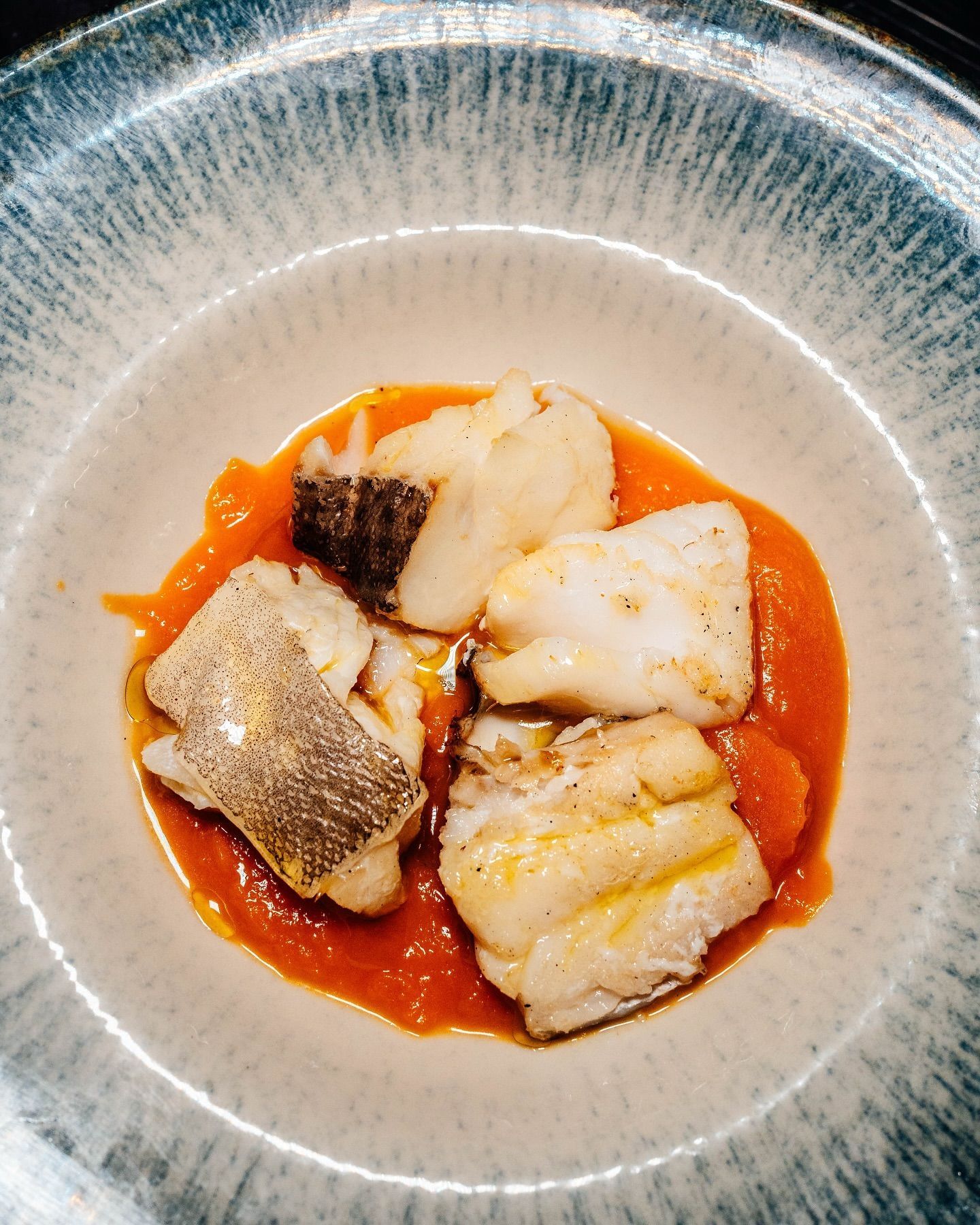 Risotto con salsa all'arancia, guarnito con due scampi su un piatto nero.